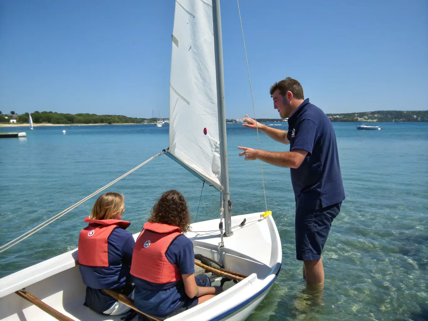 A focused sailing instructor teaching a student how to adjust the sails on a small sailboat, emphasizing hands-on learning and skill development in a training program.