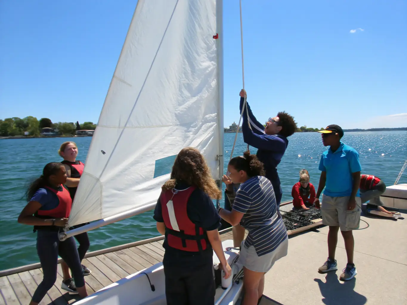 A group of club members laughing and working together to rig a sailboat at the BASE NAUTIQUE DE VIRLAY, showcasing teamwork and camaraderie.